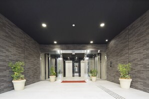 A modern hotel entrance with a brick wall, two potted plants, and an elevator. - SHIZUTETSU HOTEL PREZIO Hakata-Ekimae (Fukuoka)