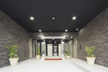 A modern hotel entrance with a brick wall, two potted plants, and an elevator.