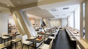 A modern dining area with multiple tables and chairs, a kitchen in the background, and a staircase leading to another level. - SHIZUTETSU HOTEL PREZIO Hakata-Ekimae (Fukuoka)