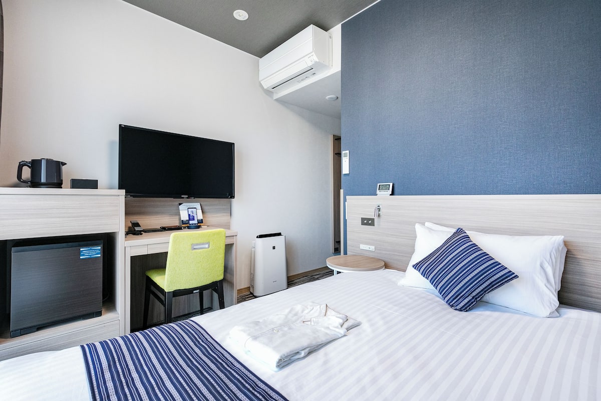 Ein Hotelzimmer mit einem Bett, einem Schreibtisch mit Computer, einem Fernseher und einer Klimaanlage.
