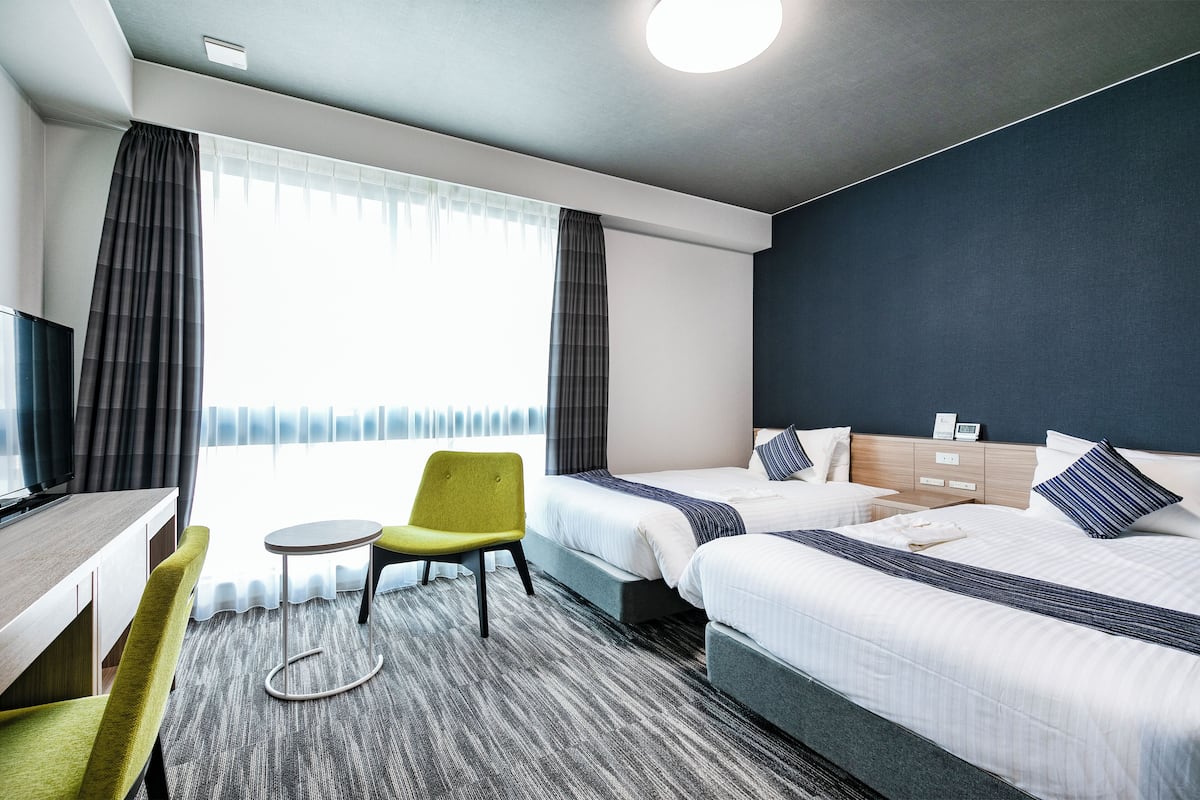 Ein Hotelzimmer mit zwei Betten, einem Schreibtisch, einem Stuhl und einem kleinen Tisch.