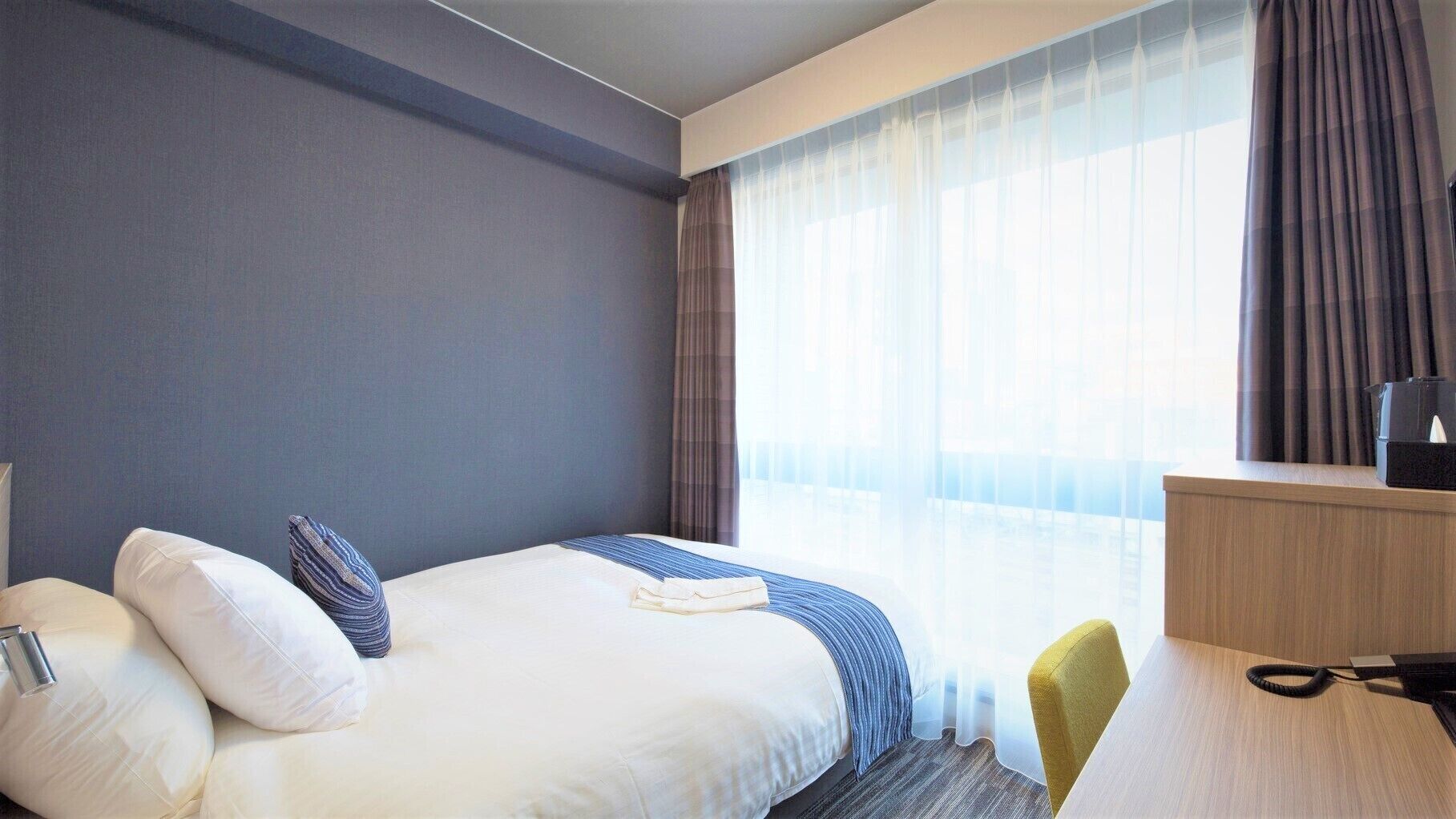Een hotelkamer met een bed, een bureau, een stoel en een raam met gordijnen.