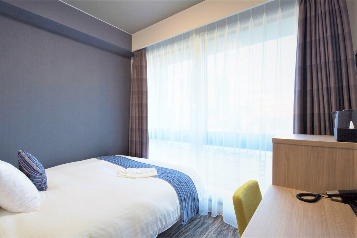 Ein Hotelzimmer mit Bett, Schreibtisch, Stuhl und einem Fenster mit Vorhängen.