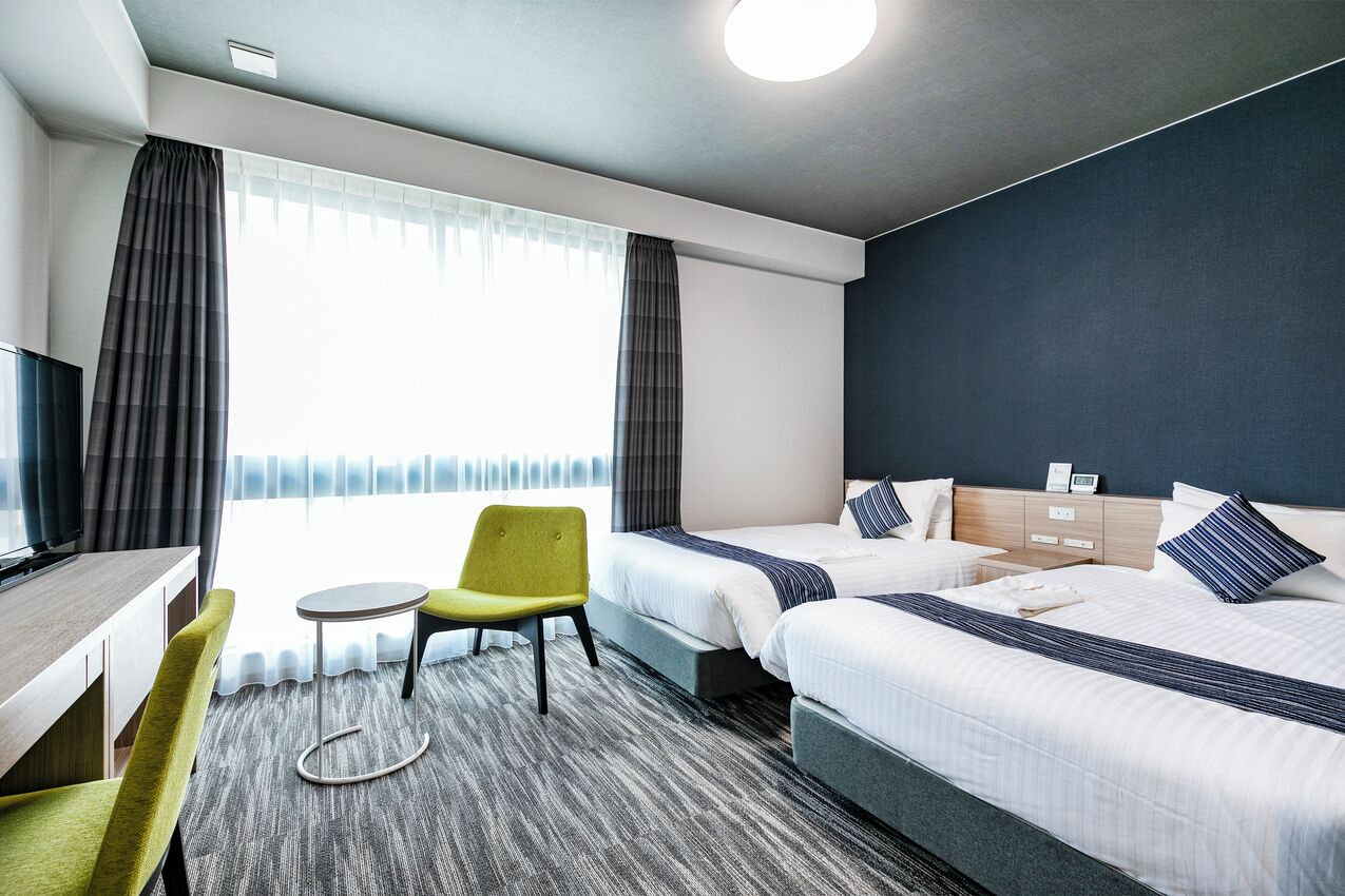 Een hotelkamer met twee bedden, een bureau, een stoel en een klein tafeltje.