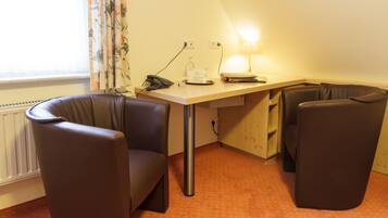 A small, triangular room with a desk, two chairs, a lamp, and a radiator.