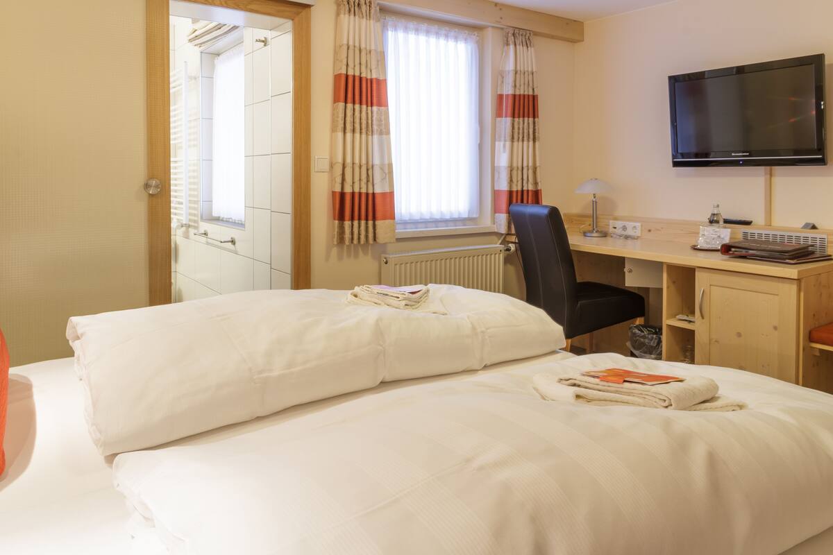 A hotel room with a bed, a desk, a chair, a television, and a window with curtains.