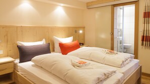 A neatly made bed with white and orange pillows, a wooden headboard, and a bedside table with a lamp. - Hotel Landgasthof Gilsbach (Winterberg)