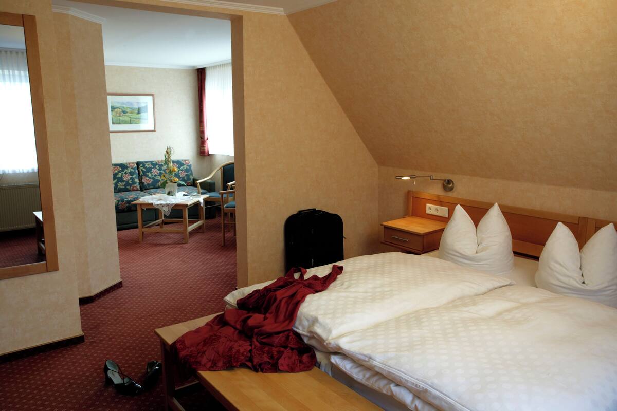 A hotel room with a bed, a wooden nightstand, a chair, a table, and a sofa.