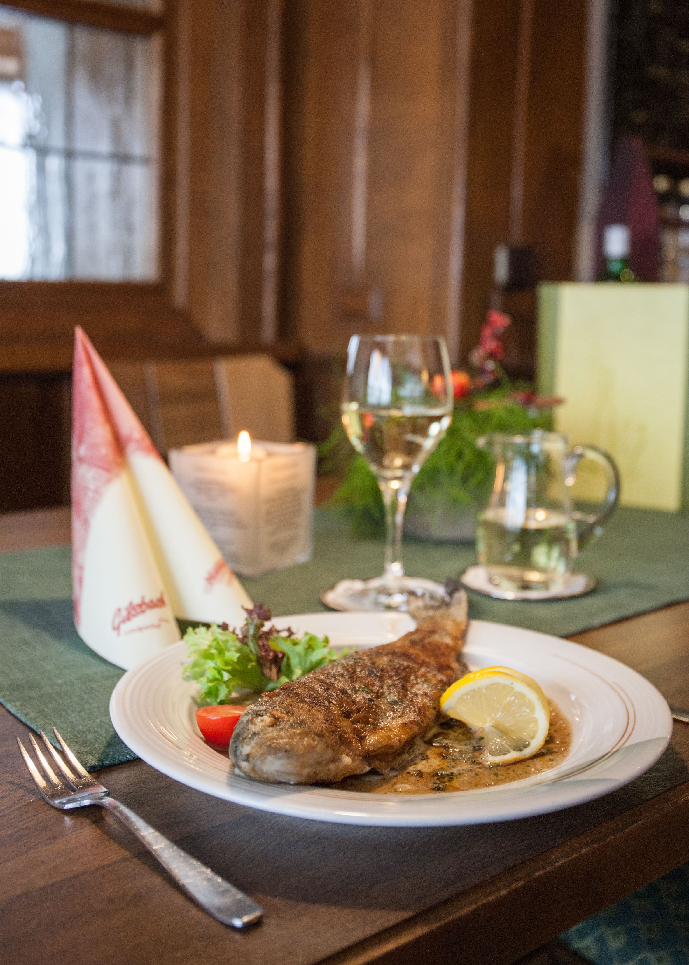 A plate with a fish, lemon, and salad on a table with a candle, glass, and pitcher.