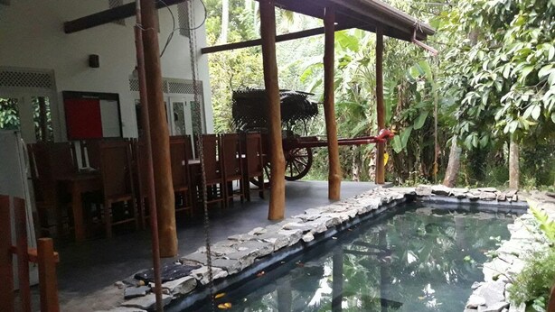 A covered outdoor area with a stone-lined pool, wooden chairs, and a rustic wooden cart.