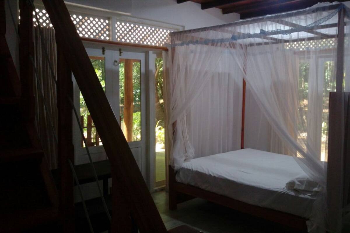 A bedroom with a four-poster bed, a wooden ladder, and a window with a white curtain.