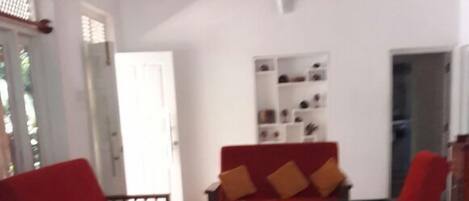 Una sala de estar con un sofá de color oscuro frente a una pared blanca, piso de madera y un sillón rojo.