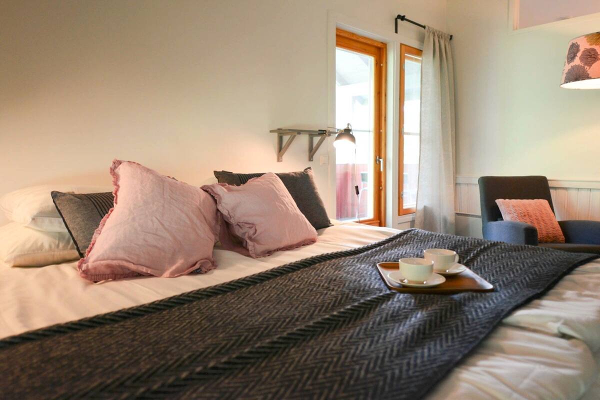 A neatly made bed with a herringbone-patterned throw, a tray with cups and saucers, and a chair with a cushion.