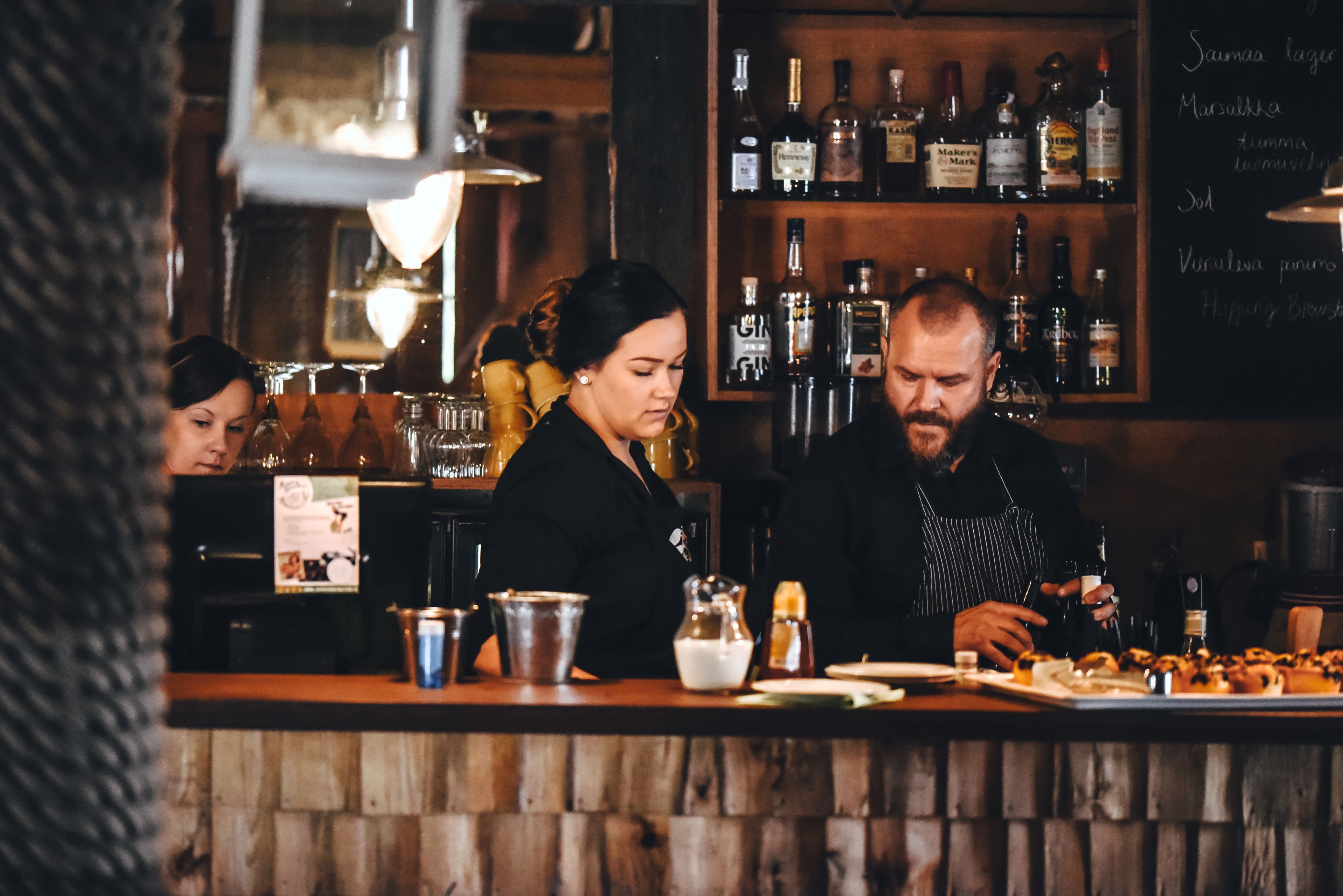 Eine Bar mit Holztresen, Regalen voller Flaschen und einer Kreidetafel mit der Speisekarte.