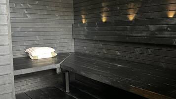 Ein kleiner, dunkler Raum aus Holz mit einer Bank und einer Metallschale auf dem Boden.