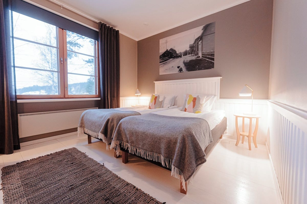 A bedroom with two beds, a large window, a radiator, and a wall-mounted picture.