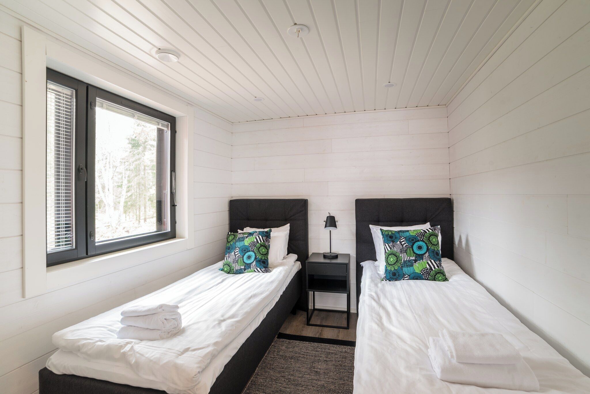A room with two single beds, a small table, and a window with blinds.