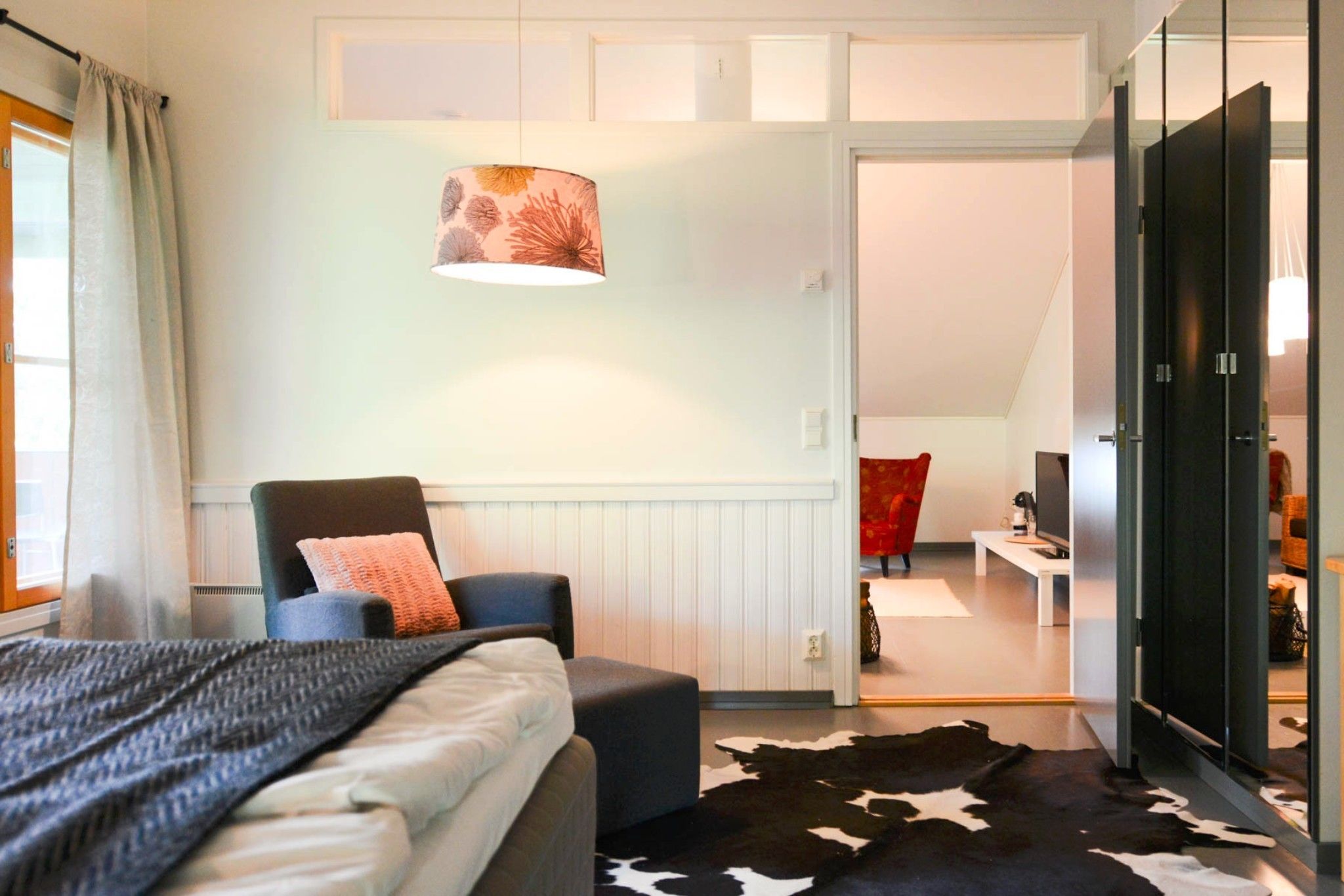 A modern bedroom with a bed, a chair, a cowhide rug, a television, and a wardrobe.