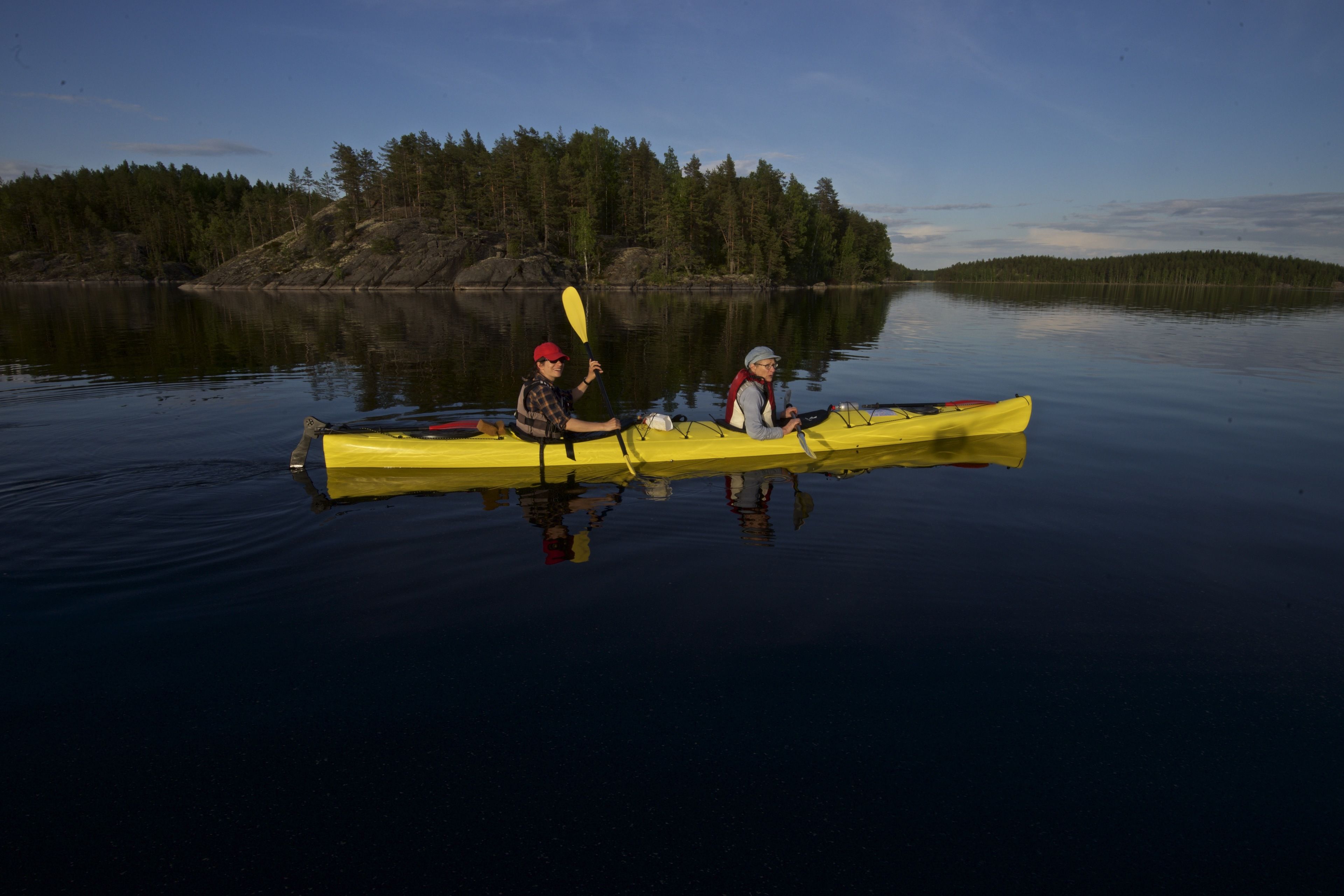 Two people in a yellow canoe on calm water with a forested island in the background.