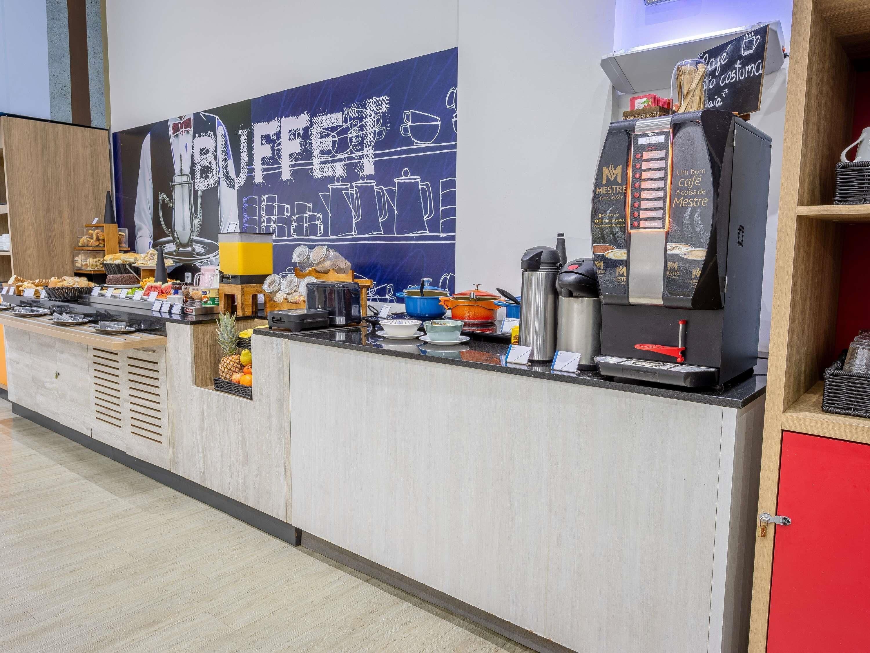 Mostrador de buffet con diversos alimentos, una máquina de café y una pizarra con escritura.