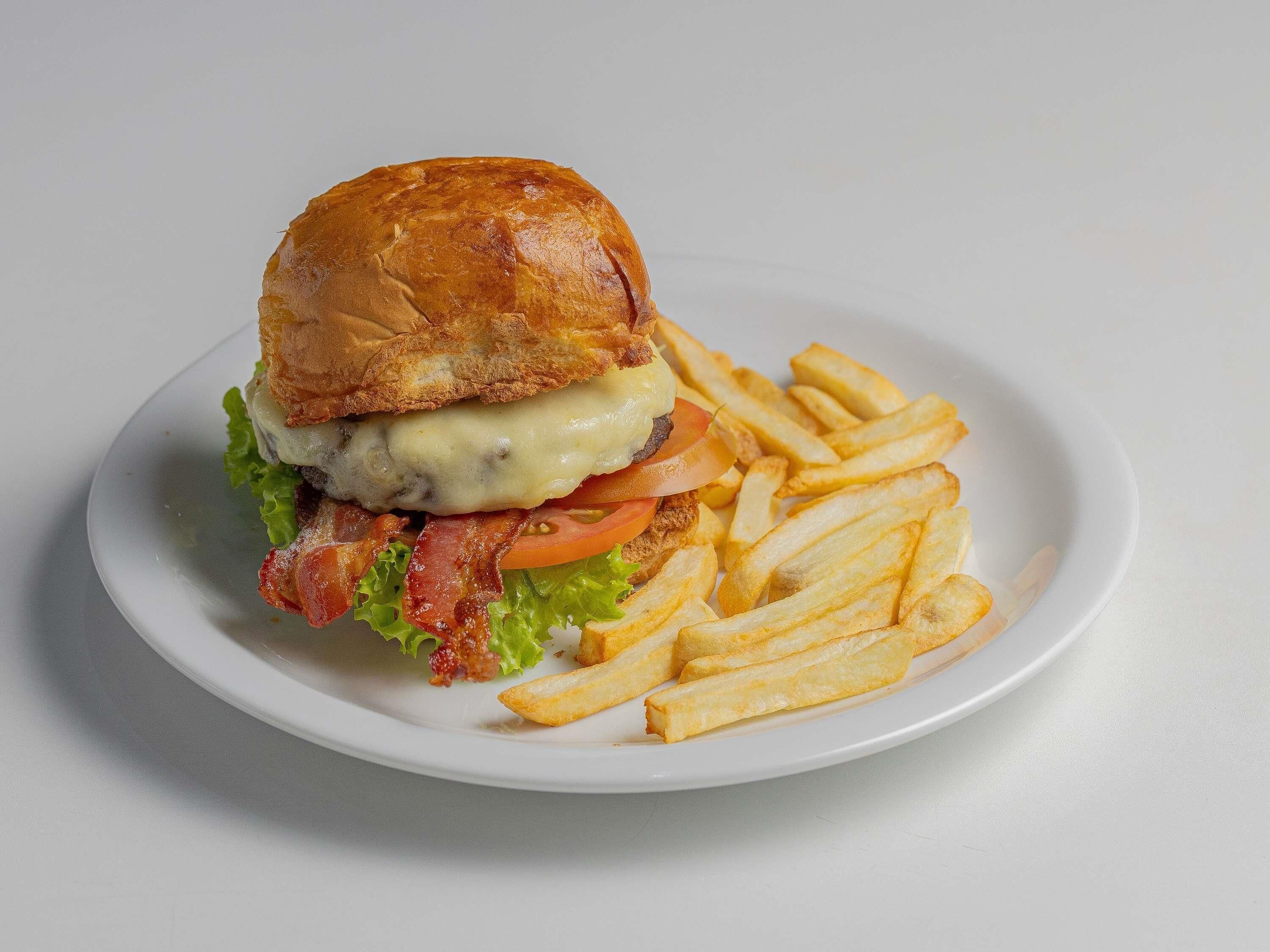 A burger with bacon, cheese, lettuce, and tomato, served with French fries on a white plate.