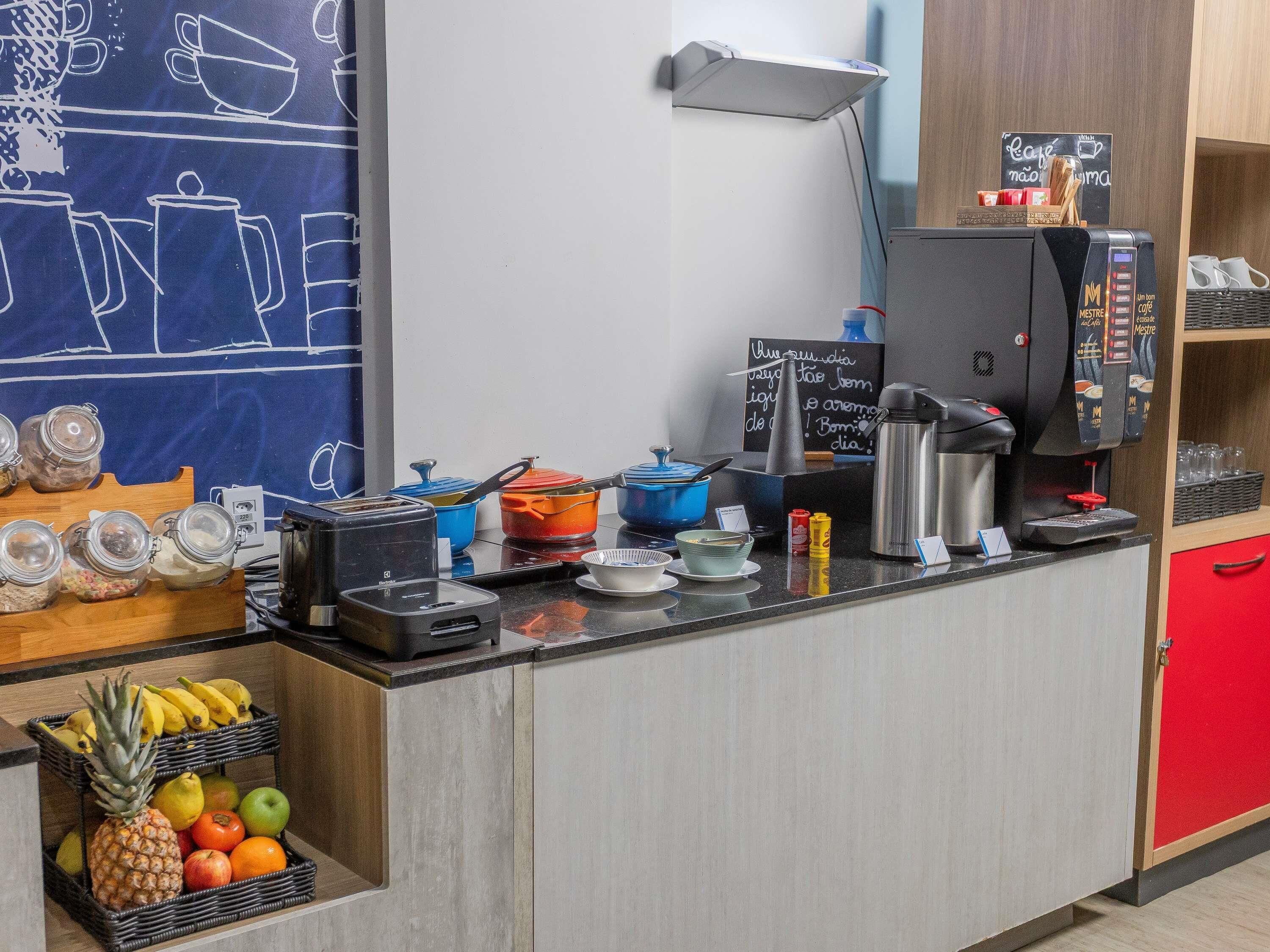 A coffee station with a coffee machine, condiment dispensers, and a chalkboard menu.