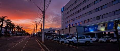 Un hotel de diseño moderno, un estacionamiento con coches y un cielo al atardecer.