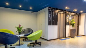 A reception area with a desk, chairs, a potted plant, and a wall with hanging decorations. - ibis budget Patos de Minas (Patos de Minas)
