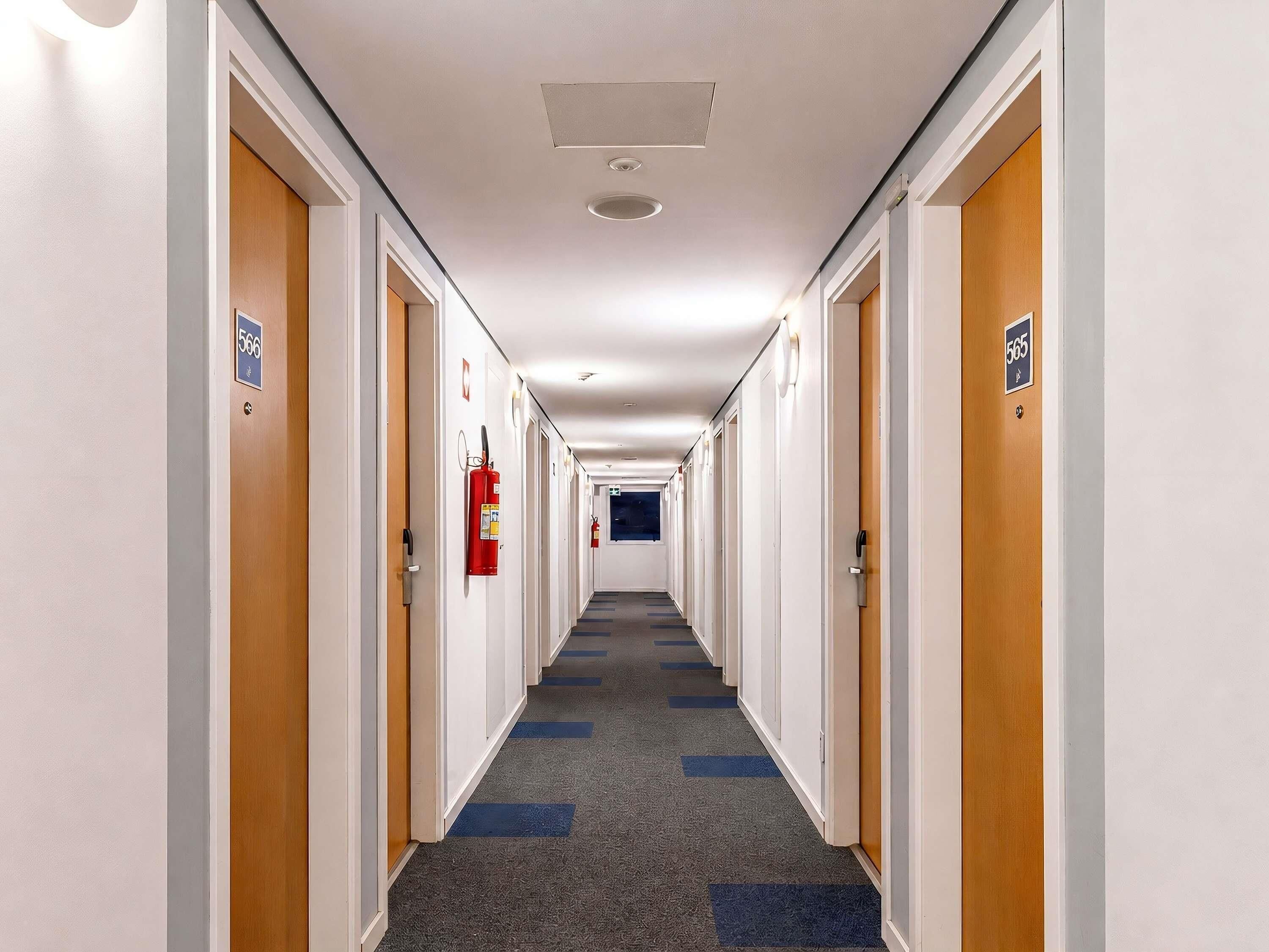 A hotel hallway with doors numbered 566 and 565, carpeted floors, and a fire extinguisher mounted on the wall.