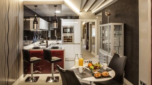 A modern kitchen with a dining area, featuring a bar with stools, a breakfast table with fruit and pastries, and a wine glass on the cabinet. - Wine & Soul Suites (Haro)