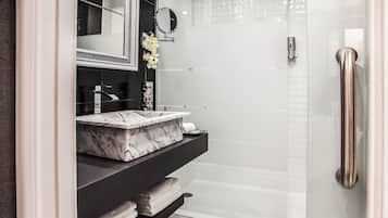 A modern bathroom with a marble sink, a glass shower enclosure, and a handrail.