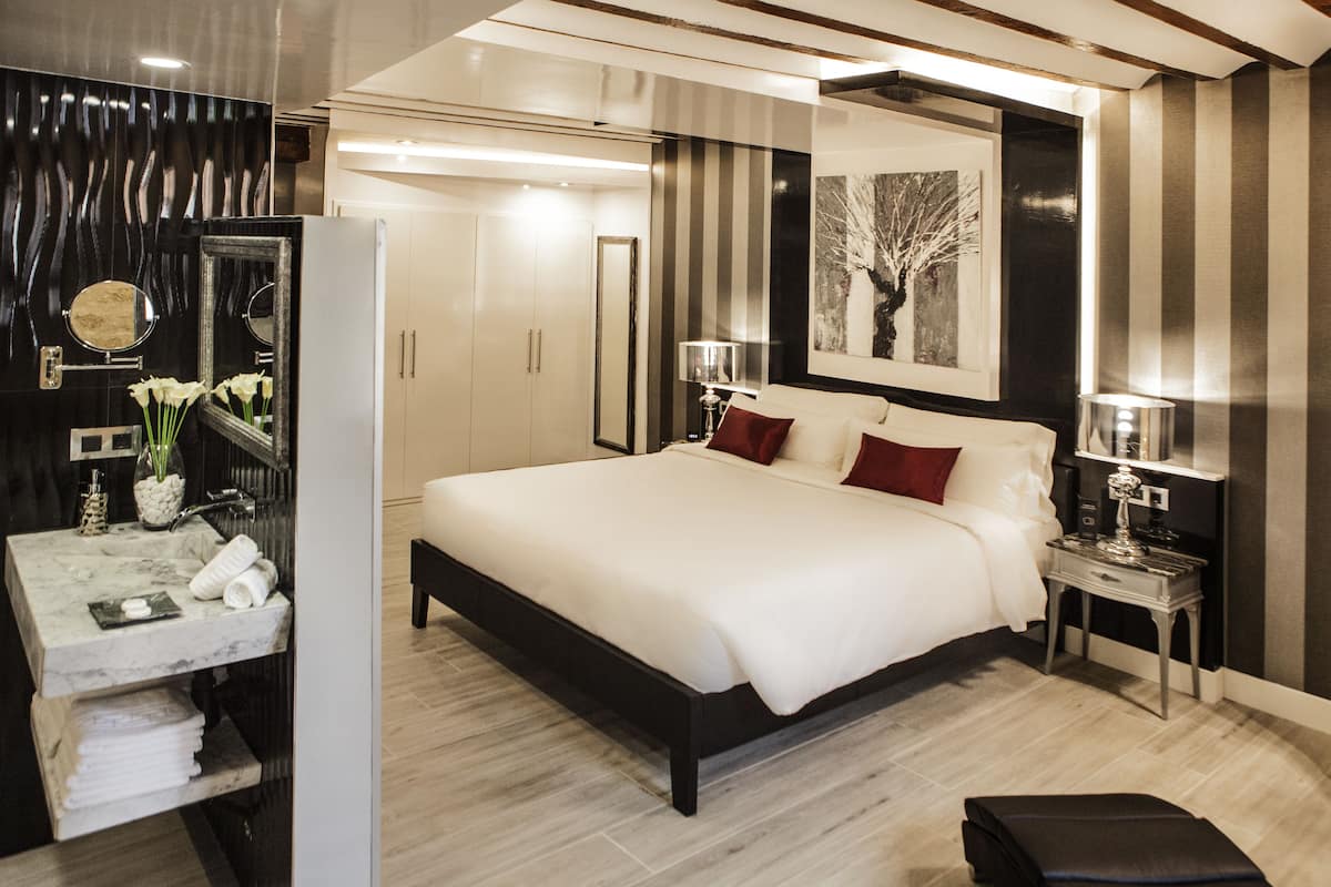A modern bedroom with a large bed, bedside tables, a vanity with a mirror, and a framed artwork on the wall.