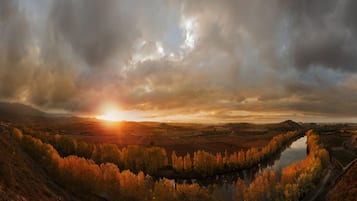 Et panoramaudsigt over en dal med en flod, omgivet af efterårsfarvede træer og fjerne bakker under en skyet himmel.