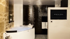 A modern bathroom with a large bathtub, a stone wall, and a sign for 'WINE & SOUL SUITES'. - Wine & Soul Suites (Haro)