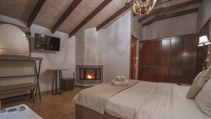 A bedroom with a large bed, a fireplace, a television, and a wooden bench. - Alkyonis Hotel & Spa (Almopia)