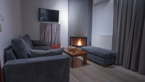 A modern living room with a fireplace, grey sofas, a coffee table, and a television mounted on the wall. - Alkyonis Hotel & Spa (Almopia)
