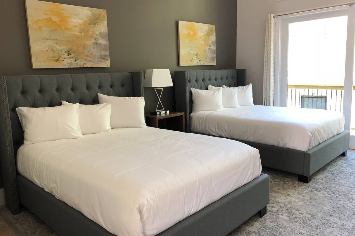 A hotel room with two beds, a grey headboard, white bedding, and abstract paintings on the wall.