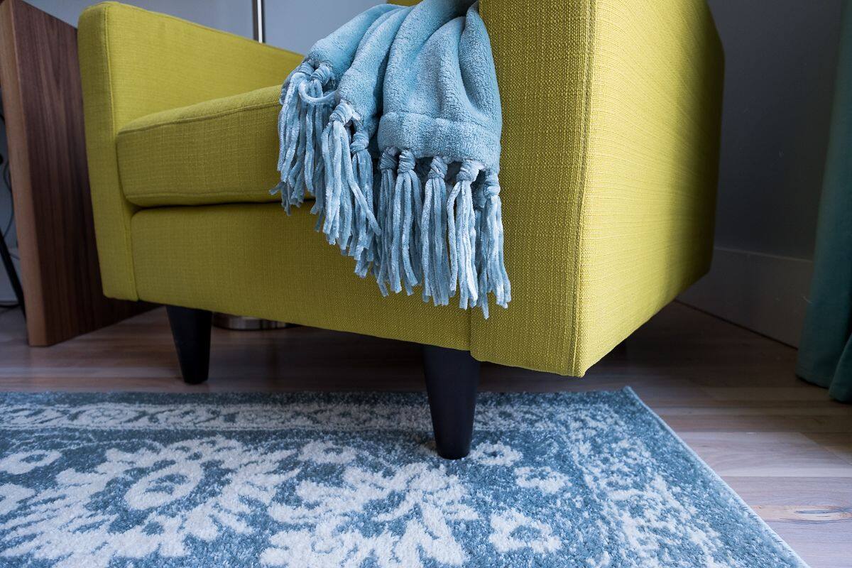 A yellow armchair with a blue fringed throw blanket, positioned on a patterned blue and white rug.