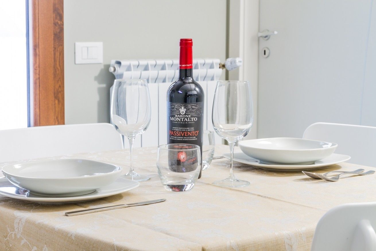 Una mesa dispuesta con una botella de vino Barone Montalto Passivento, dos copas de vino, y platos y cubiertos blancos.