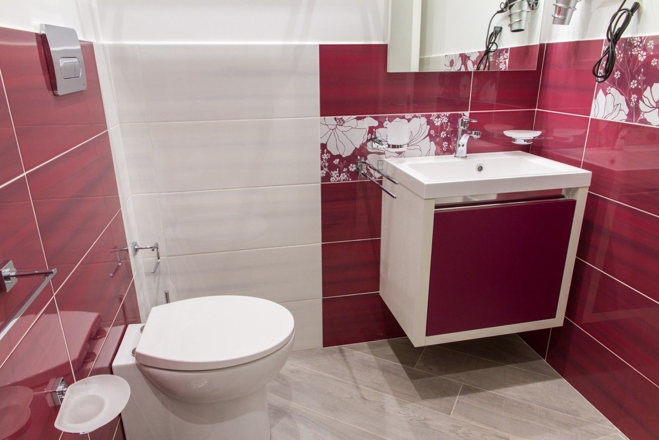 Ein Badezimmer mit Toilette, Waschbecken und Spiegel sowie roten und weißen Fliesen an den Wänden.