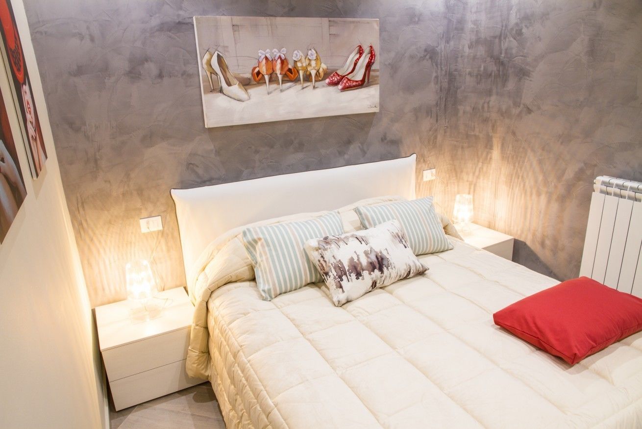 A bedroom with a large bed, a headboard, two bedside tables, and a wall-mounted artwork of shoes.