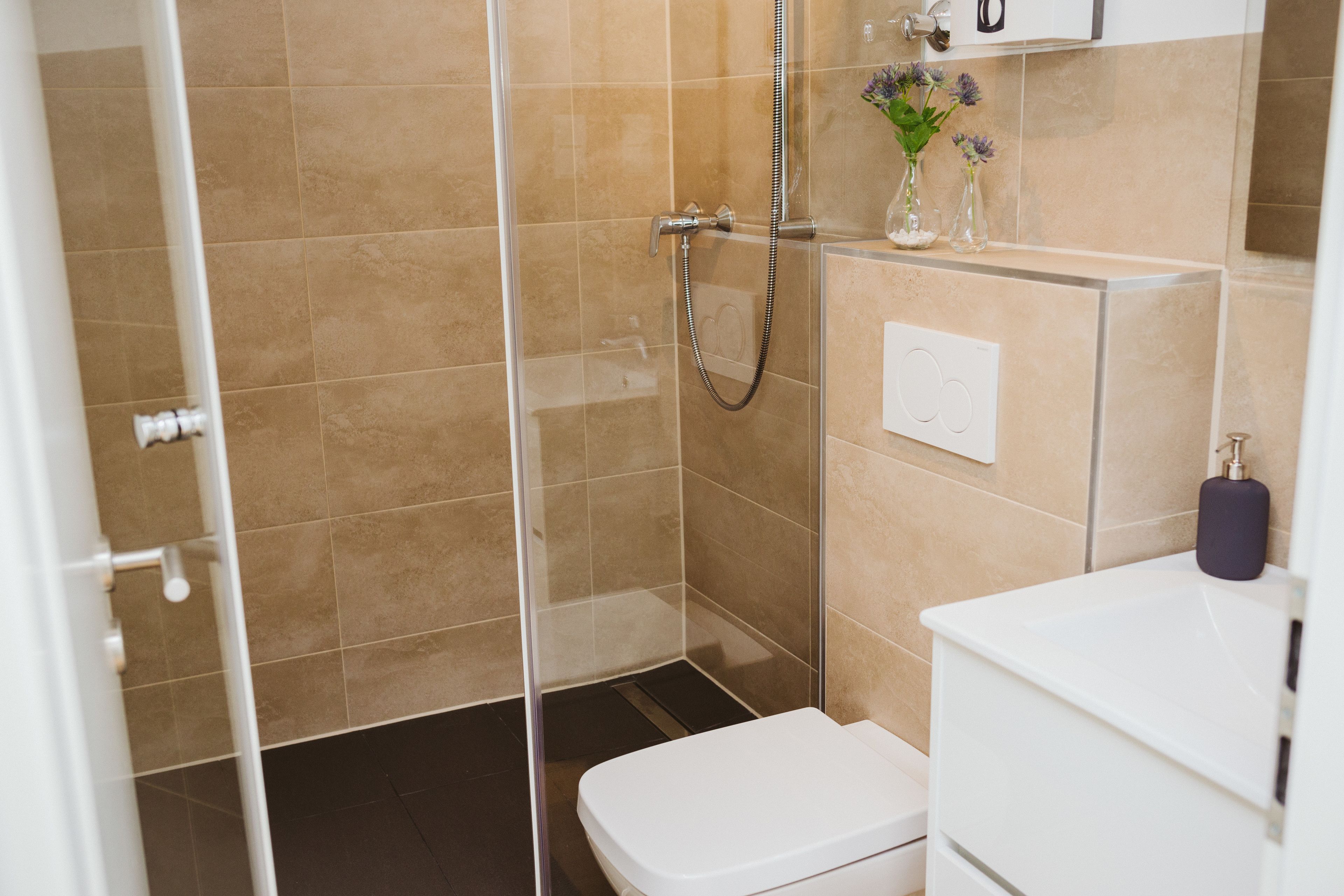 Ein modernes Badezimmer mit einer Glaskabine zur Dusche, einer weißen Toilette und einem Waschbecken mit Spiegel.