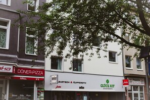 Un immeuble abritant un restaurant de « döner-pizza », des appartements « Bartsch & Kupferoth » et une enseigne « Glück Auf ».