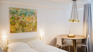 A hotel room with a bed, a round table with chairs, a painting on the wall, and a hanging light fixture. - Glück Auf Appartements Rüttenscheiderstraße (Essen)