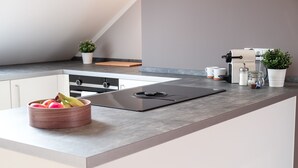A modern kitchen with a built-in stove, a bowl of fruit, a coffee maker, and potted plants. - Glück Auf Appartements Rüttenscheiderstraße (Essen)