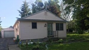 Een gelijkvloers huis met een veranda, een garage en een kleine tuin.