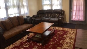 Een woonkamer met een bruine leren bank, een houten salontafel en een kamerkleed met een patroon.