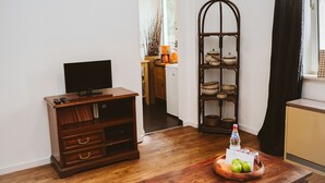 A living room with a wooden entertainment center, a television, a wooden coffee table with a bowl of apples and a bottle of water, and a decorative shelf with bowls. - Glück Auf Appartements See Straße (Essen)