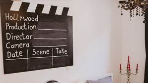 A bedroom with a bed, a bedside table, a lamp, a chandelier, a candelabra, and a chalkboard with Hollywood Production details. - Glück Auf Appartements See Straße (Essen)