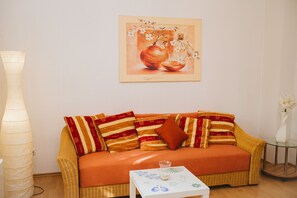 A cozy room with a wicker sofa, striped cushions, a small table with a glass, and a framed artwork on the wall. - Glück Auf Appartements See Straße (Essen)